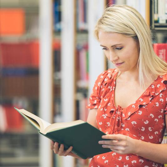 Library user reading bound volume, Background bookshelves